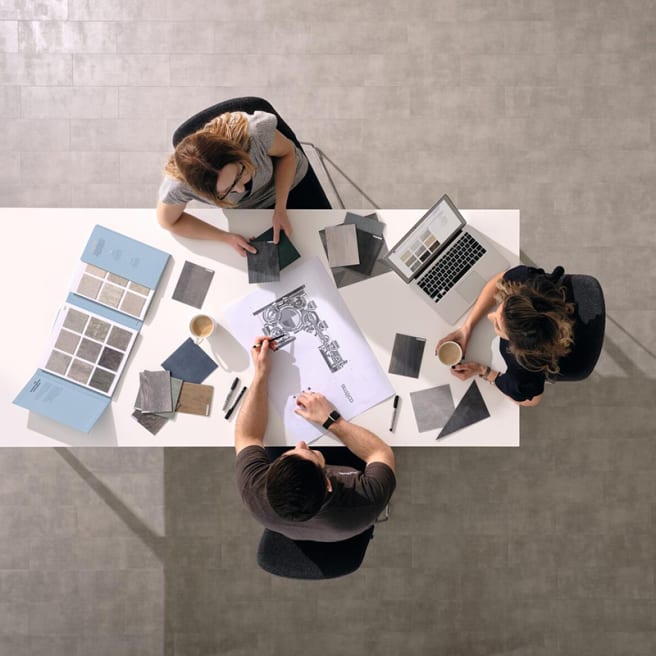 Top down view of three people sat around a table with flooring samples and plans