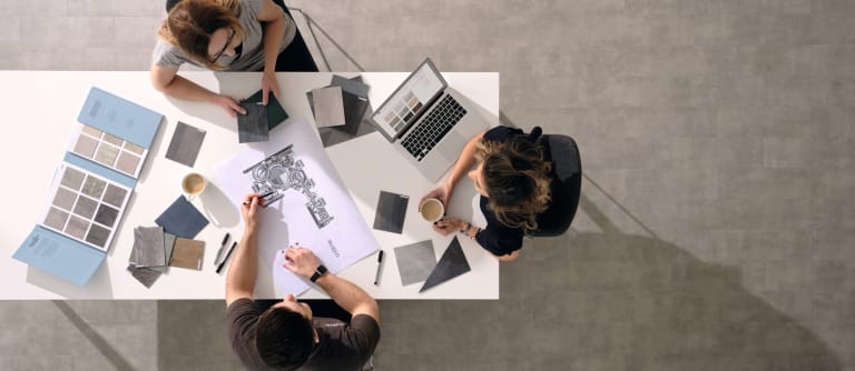 Top down view of three people sat around a table with flooring samples and plans